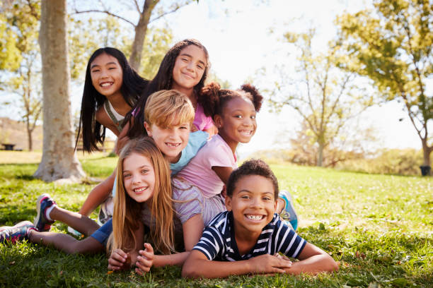 Multi-ethnic group of kids lying on each other in a park Multi-ethnic group of kids lying on each other in a park mixed racial group of friendly children laughing together stock pictures, royalty-free photos & images