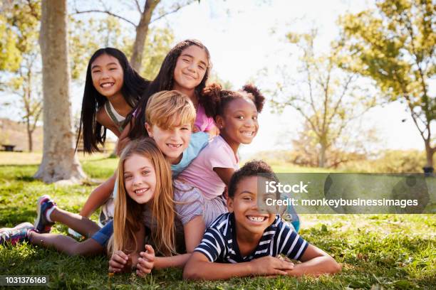 Foto de Multiétnica Grupo De Crianças A Mentir Uns Aos Outros Em Um Parque e mais fotos de stock de Criança