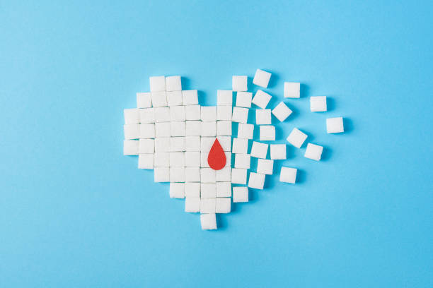 a drop of blood on broken heart made of pure white cubes of sugar isolated on blue background, World diabetes day stock photo