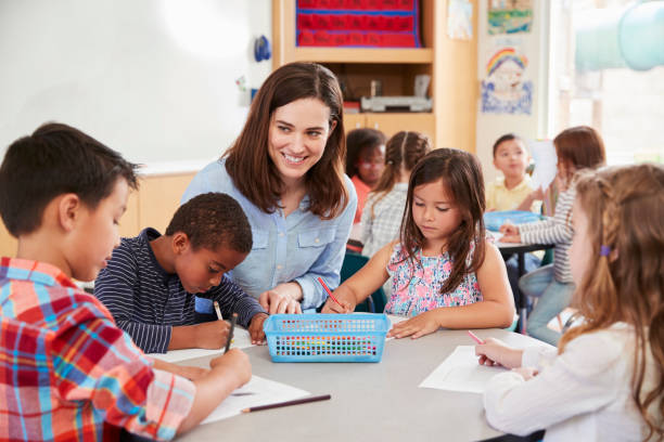 istock Teacher sitting at table with young school kids in classroom 1031377386