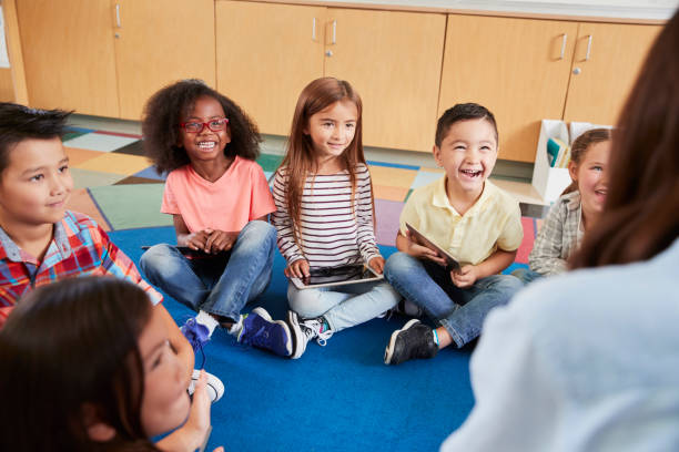 istock Elementary school kids sitting on floor looking at teacher 1031377558