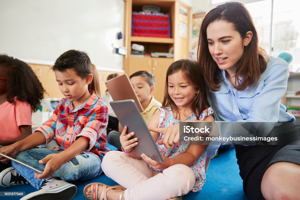 Teacher helps girl in elementary class with tablet computers Teacher Stock Photo