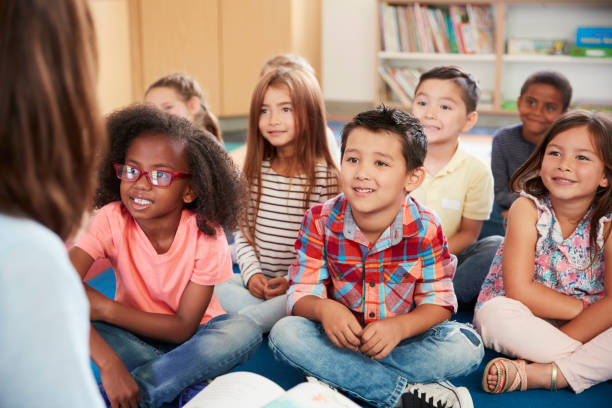 istock Elementary school kids sit on floor looking up at teacher 1031377754
