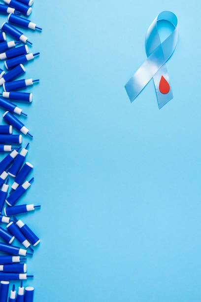 blue ribbon awareness with red blood drop and line of lancets on a blue background, World diabetes day stock photo