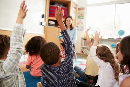 Vista posterior de los niños de escuela primaria levantando manos al maestro, photo
