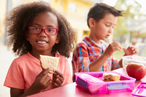 Young school girl and boy with packed lunches look to camera Young school girl and boy with packed lunches look to camera food elementary student healthy eating schoolboy stock pictures, royalty-free photos & images