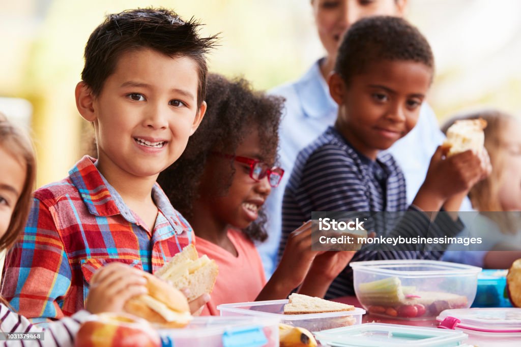 Les enfants d’âge scolaire manger paniers repas ensemble autour d’une table - Photo de Enfant libre de droits