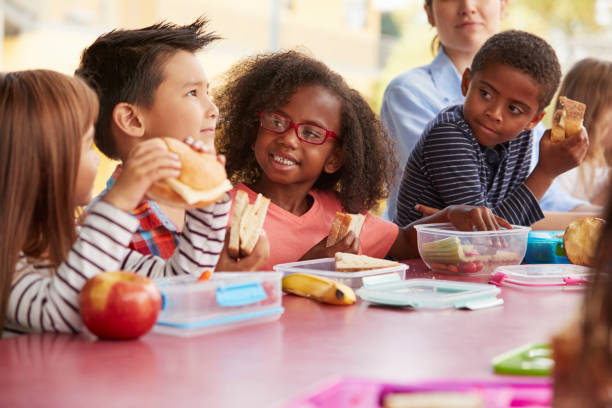 junge schule kinder beim mittagessen an einem tisch miteinander reden - mittagessen stock-fotos und bilder