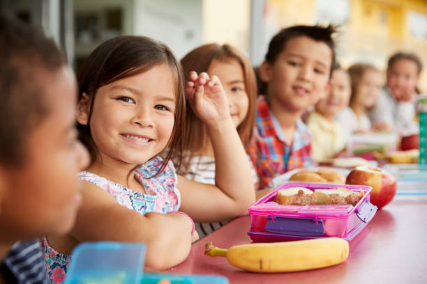 bambini delle scuole elementari seduti un tavolo con pranzi al sacco - childrens food foto e immagini stock