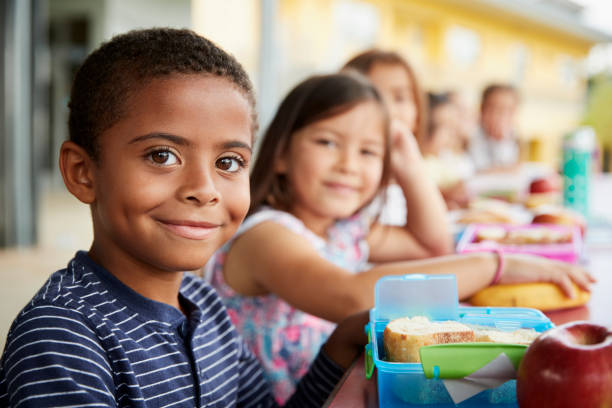 niño y niña en la mesa del almuerzo de escuela sonriendo a la cámara - comida del mediodía fotos fotografías e imágenes de stock