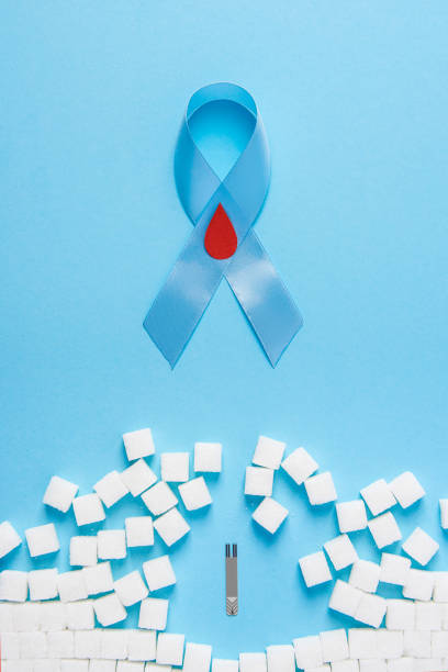 blue ribbon awareness with red blood drop and wall made of sugar cubes ruined by Glucose Test Strips on blue background stock photo