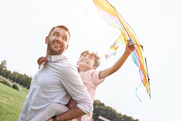 istock Weekend activities. Father carrying son on his back holding kite walking on field in nature smiling happy 1031380690