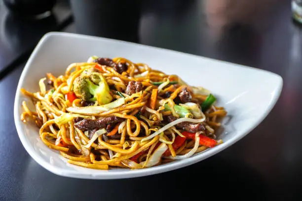 Chinese Noodles with Sliced Beefs with Fresh Vegetables served on a White Plate.