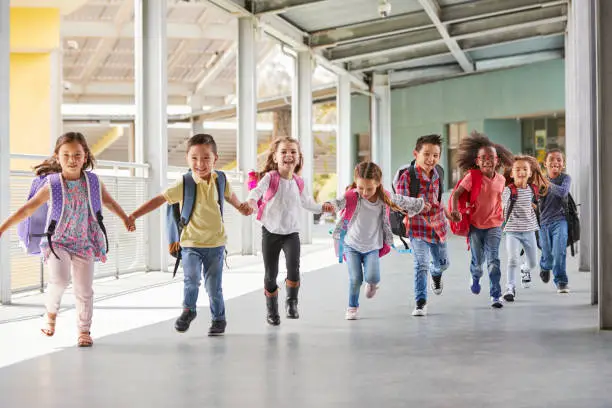Photo of Primary school kids run holding hands in corridor, close up