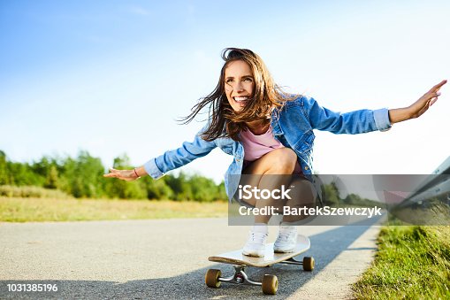 istock Smiling woman riding longboard in countryside during summer 1031385196