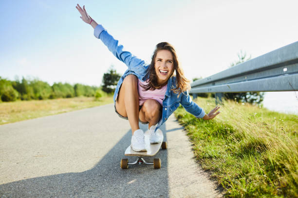 istock Laughing woman riding longboard with arms raised 1031385374