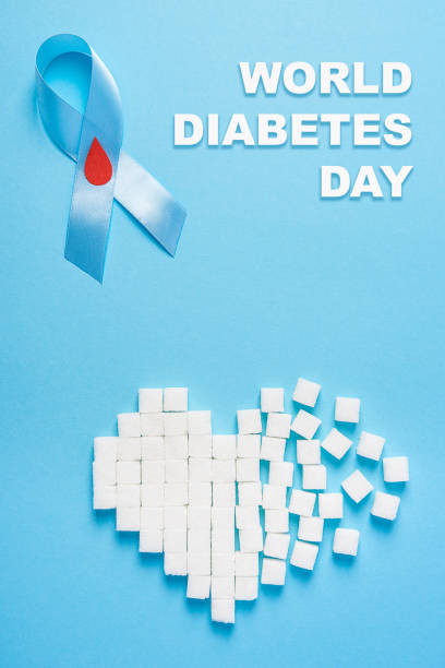 inscription world diabetes day, blue ribbon awareness with red blood drop, broken heart of sugar cubes, blue background stock photo