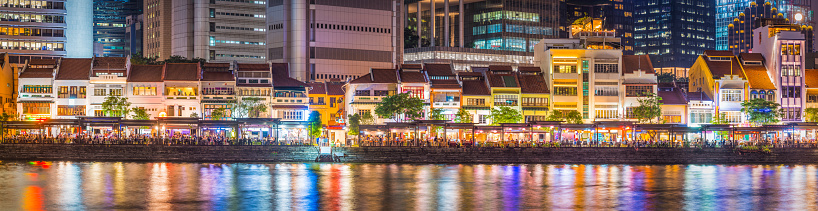 The warm lights of the crowded restaurants and bars of Boat Quay illuminated beside the river in central Singapore.