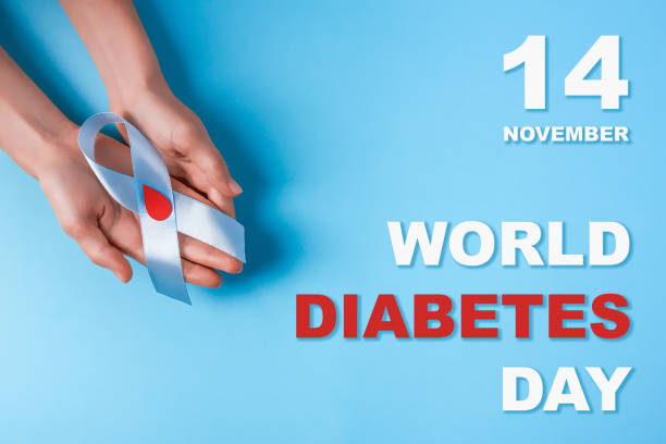inscription world diabetes day and blue ribbon awareness with red blood drop in woman hands on a blue background stock photo