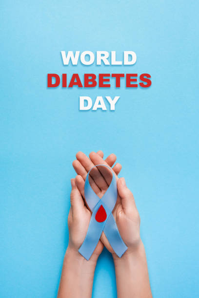 inscription world diabetes day and blue ribbon awareness with red blood drop in woman hands on a blue background stock photo