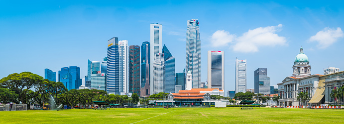 The gleaming modern skyscrapers of the  Downtown Core soaring over the historic green Padang playing fields and historic colonial architecture in the heart of Singapore.
