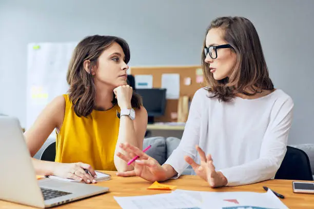 Photo of Discussing business matters. Two attractive young coworkers talking about their startup business in office