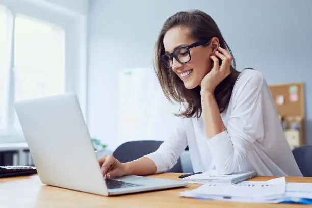 Photo of Portrait of beautiful cheerful young businesswoman working on laptop and laughing in home office