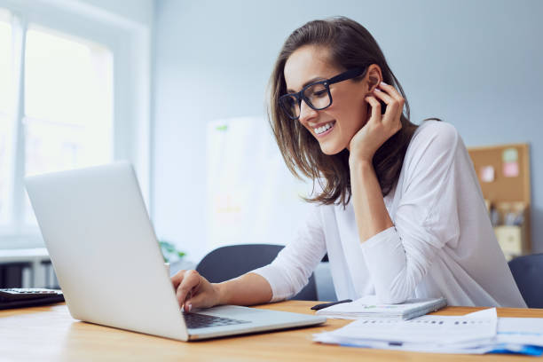 portret pięknej wesołej młodej bizneswoman pracującej na laptopie i śmiejącej się w domowym biurze - lone female zdjęcia i obrazy z banku zdjęć