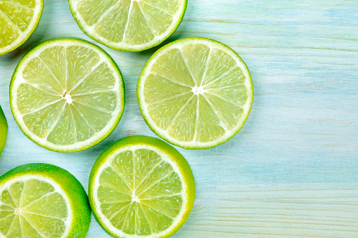 An overhead photo of many vibrant lime slices on a teal blue background