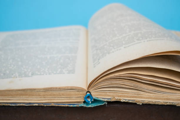 istock Close up opened vintage retro book page with blurry text for education and publication concept on blue background. Focus on book binding. Knowledge, studies, learning, university concept 1031404284