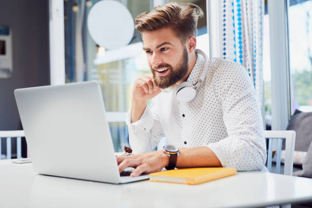 Handsome young man working on laptop while sitting in modern cafeteria