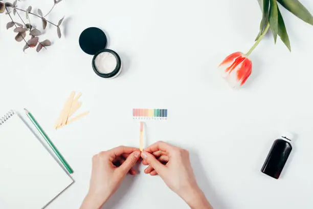 Photo of Woman testing cosmetics pH level by using litmus paper