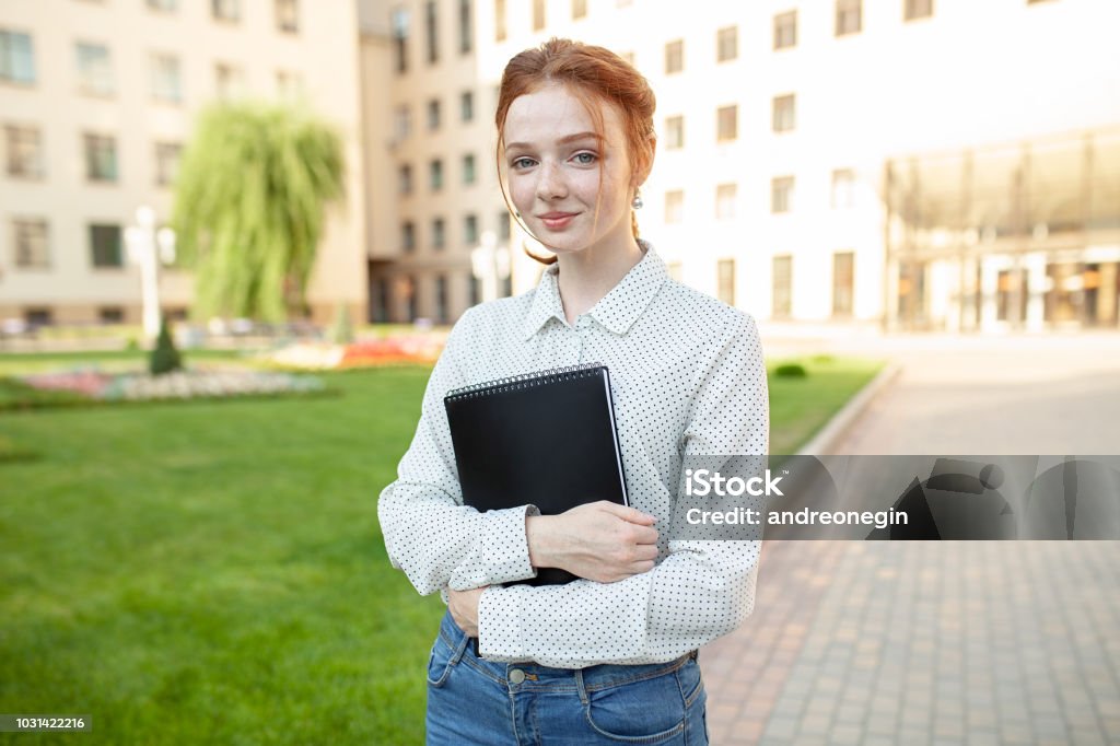 Beautiful red haired girl with freckles hugging notebooks with homework and smiling happy. Back to school concept. Portrait of a student Beautiful red haired girl with freckles hugging notebooks with homework and smiling happy. Back to school concept. Portrait of a student. Teenage Girls Stock Photo