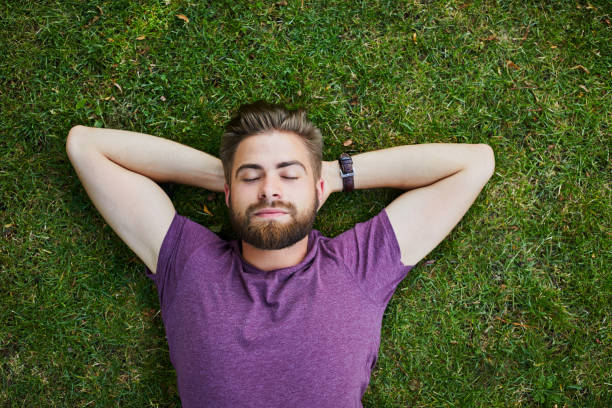 junger mann liegend am boden im park im freien mit augen geschlossen - resting place stock-fotos und bilder