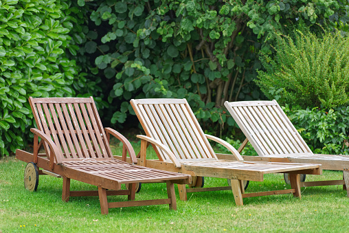 Three wooden relax loungers on a green lawn with a hedge in the background