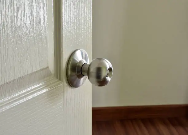 Close up of stainless metal door knob on a white painted door opening into a room.