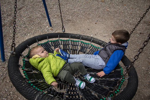 Two little boys lying down on the swing and enjoying.