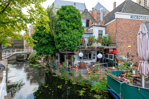 Delft, the Netherlands - Aug 21, 2018 : A cozy terrace on the water and a terrace boat in the canal, corner of two canals Vrouwenrecht-Voldersgracht, in the center of Delft, the Netherlands.