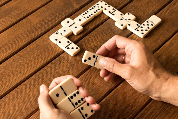 Playing dominoes on a wooden table. Man's hand with dominoes Playing dominoes on a wooden table. Man's hand with dominoes. domino stock pictures, royalty-free photos & images