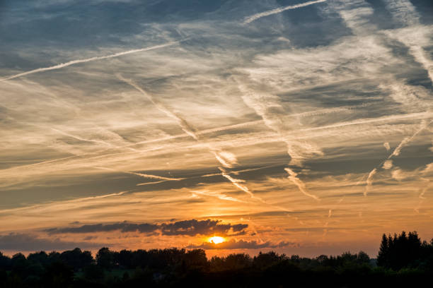 sunset in august in the belgium ardennes with clouds and lot of stripes from the planes in the sky and the red orange sun going under.