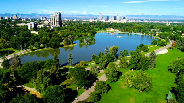 Large Pond reflecting the Denver Colorado Skyline cityscape and surrounding trees at City Park aerial drone view