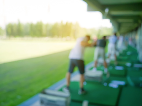 Blurred people playing golf in golf driving range