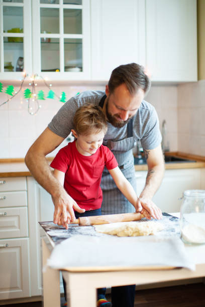 père et fils, fabrication de biscuits pour noël - rolling dough pastry apron photos et images de collection