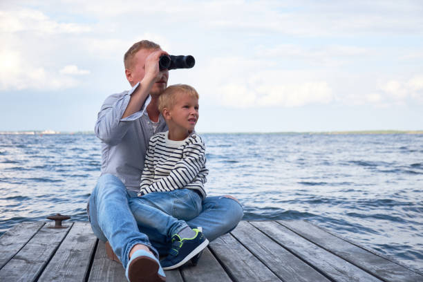 Father holding his little son looking through binoculars stock photo