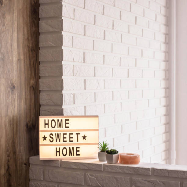 istock Home sweet home - it is written on a decorative frame with illumination in the interior between a white brick wall and a brown wooden one next to succulents and a pink candlestick. Details and decor of the interior. Copyspace 1031478920
