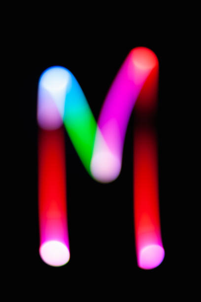 istock Letter M. Glowing letters on dark background. Abstract light painting at night. Creative artistic colorful bokeh. New Year. Use it for build you own design for book cover, CD, poster or post card. 1031481840