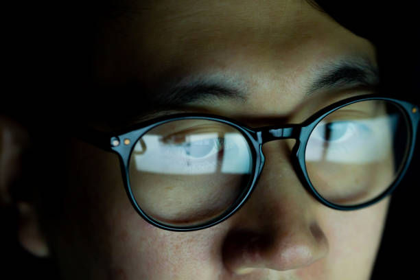 close up of young asian man in glasses watching videos and surfing internet on technology device in the dark. - human face chinese ethnicity close up men imagens e fotografias de stock
