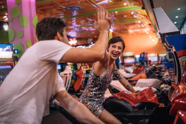 Photo of Couple playing racing games sitting on arcade racing bikes