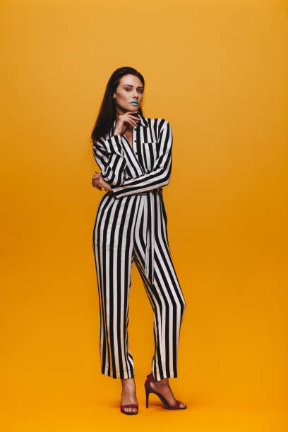 Attractive woman in striped jumpsuit Full length portrait of female fashion model standing over orange background. Attractive woman with vivid make up in striped jumpsuit posing in studio. jumpsuit stock pictures, royalty-free photos & images