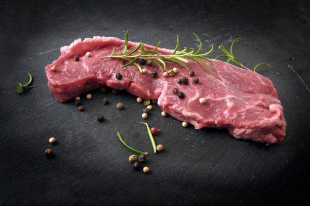 istock raw entrecote steak with rosemary and pepper on a black slate board, copy space 1031511340
